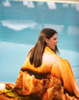 Woman sitting by a pool with the Original Chick-fil-A® Chicken Sandwich Towel draped over her shoulders
