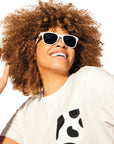 Woman with curly brunette hair wearing Cow Print Pocket Tee and Spotted Sunglasses