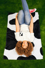 Woman laying  on black and white cow print Laze and Graze Beach Towel