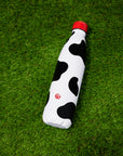 Black and white cow print Insulated Water Bottle with red lid shown on green turf