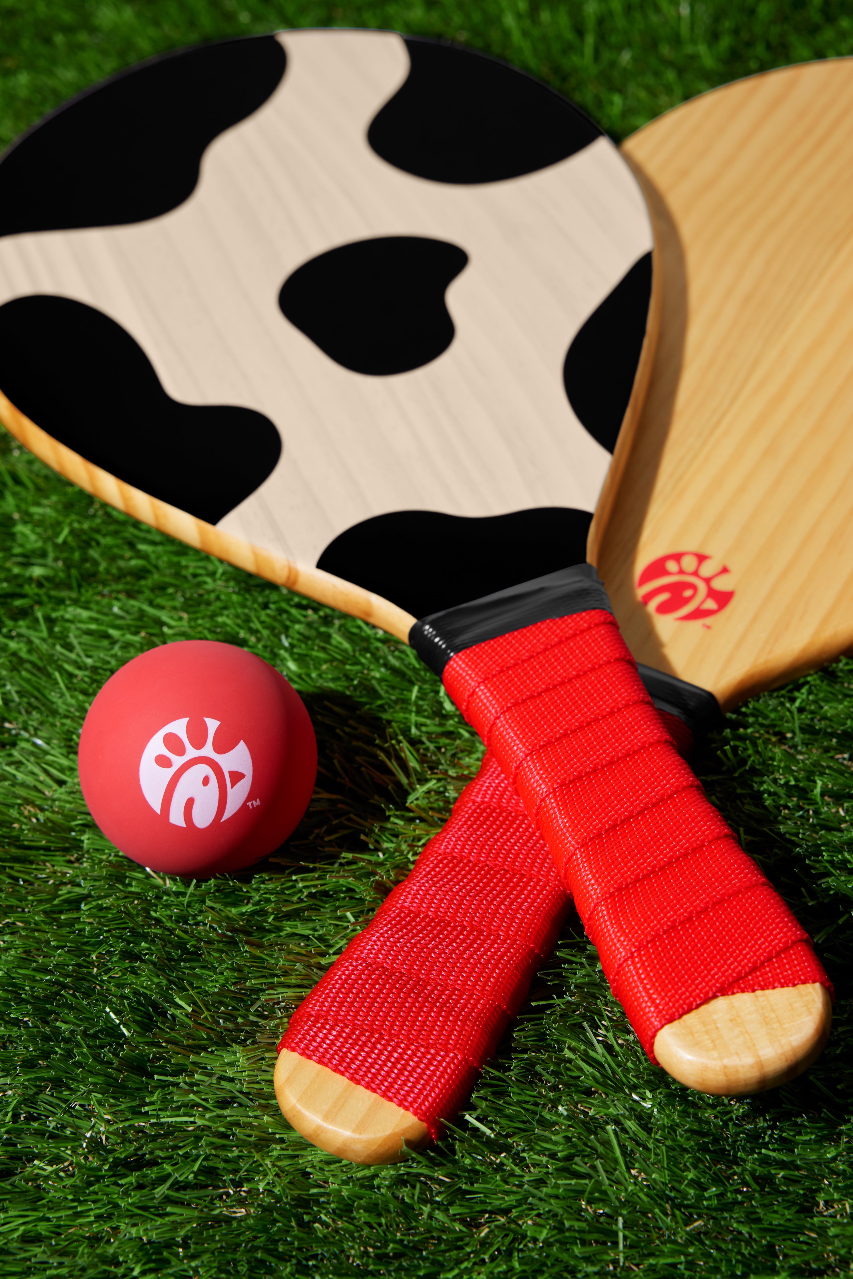 Photograph of wooden Paddle Ball Set including 2 cow print paddles and red ball on green turf