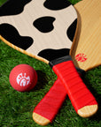 Photograph of wooden Paddle Ball Set including 2 cow print paddles and red ball on green turf