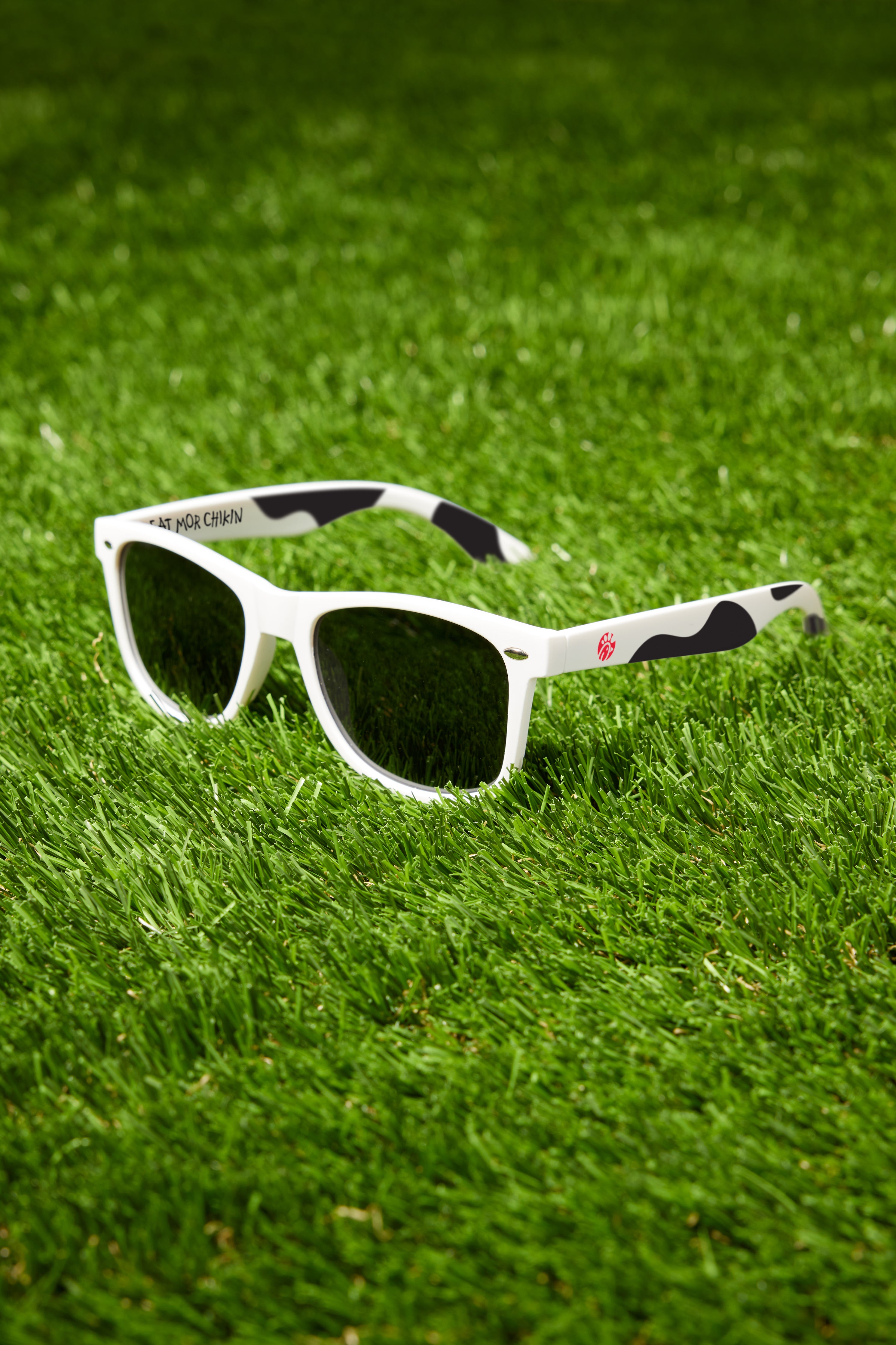 Black and white cow print sunglasses with "Eat Mor Chicken" printed on the inside of arm on sunglasses 