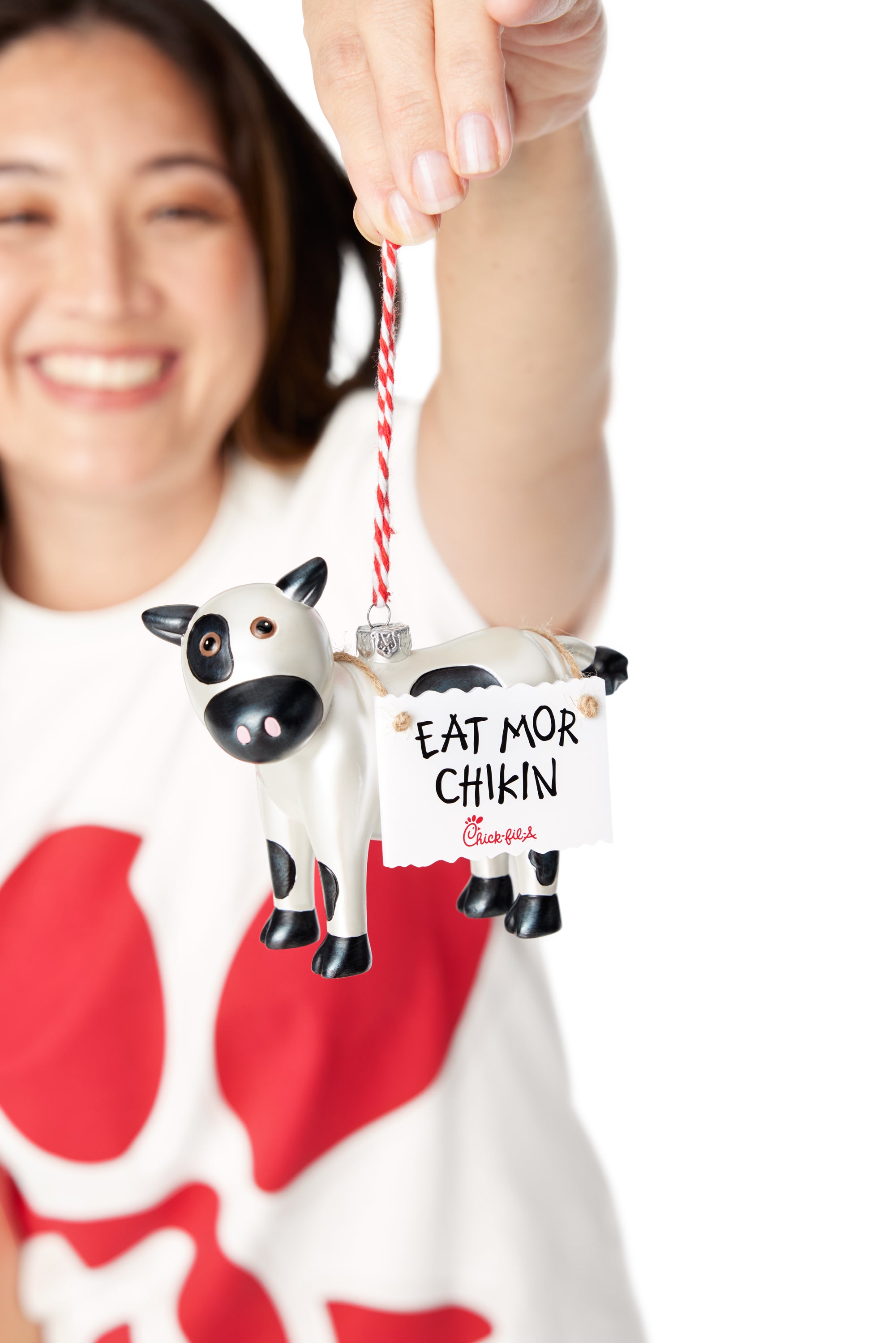 Woman in a Chick-fil-A Logo Print Tee holding a black and white cow ornament wearing a sign that says "EAT MOR CHIKIN"