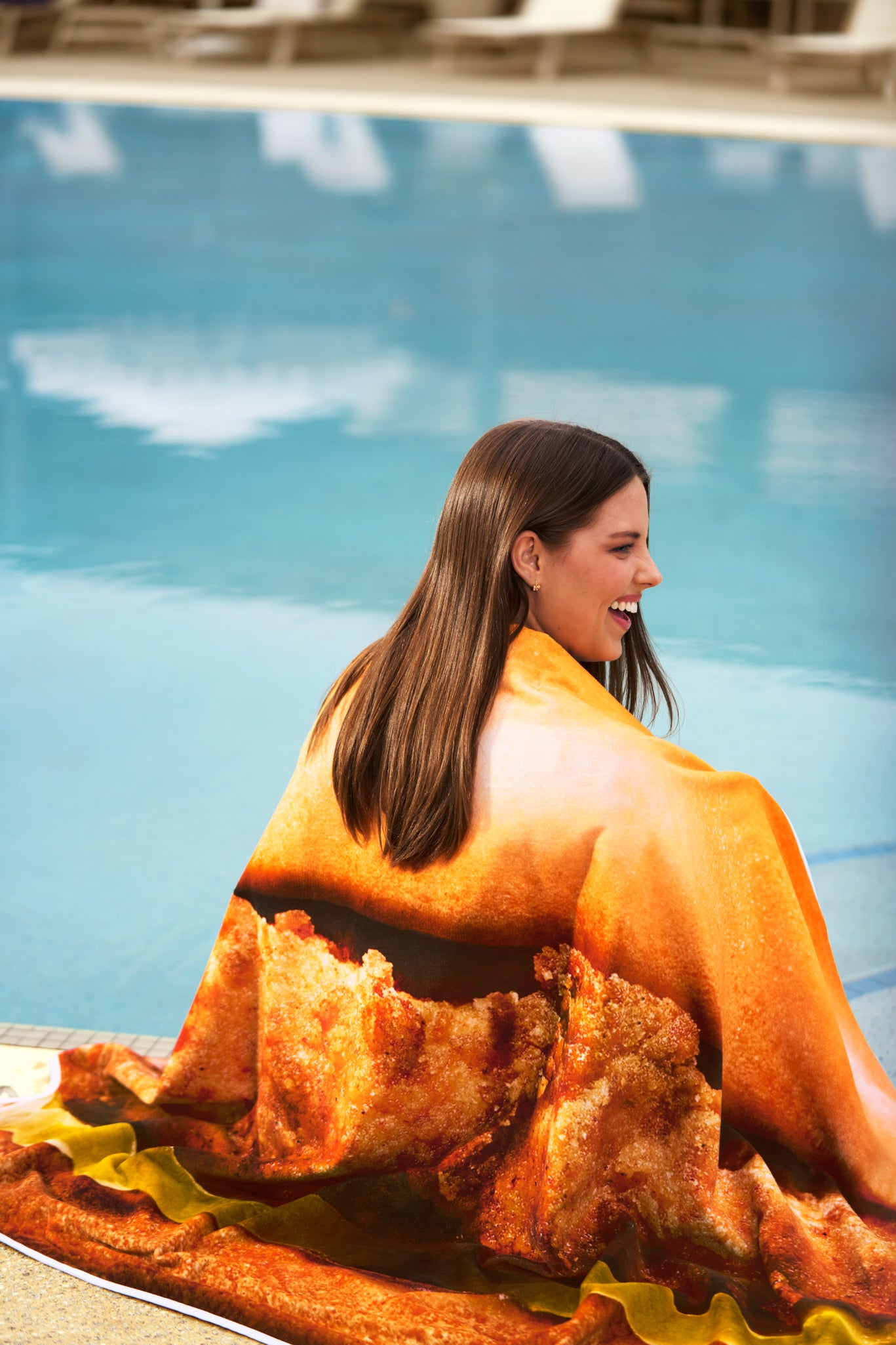 Woman sitting by a pool with the Original Chick-fil-A® Chicken Sandwich Towel draped over her shoulders