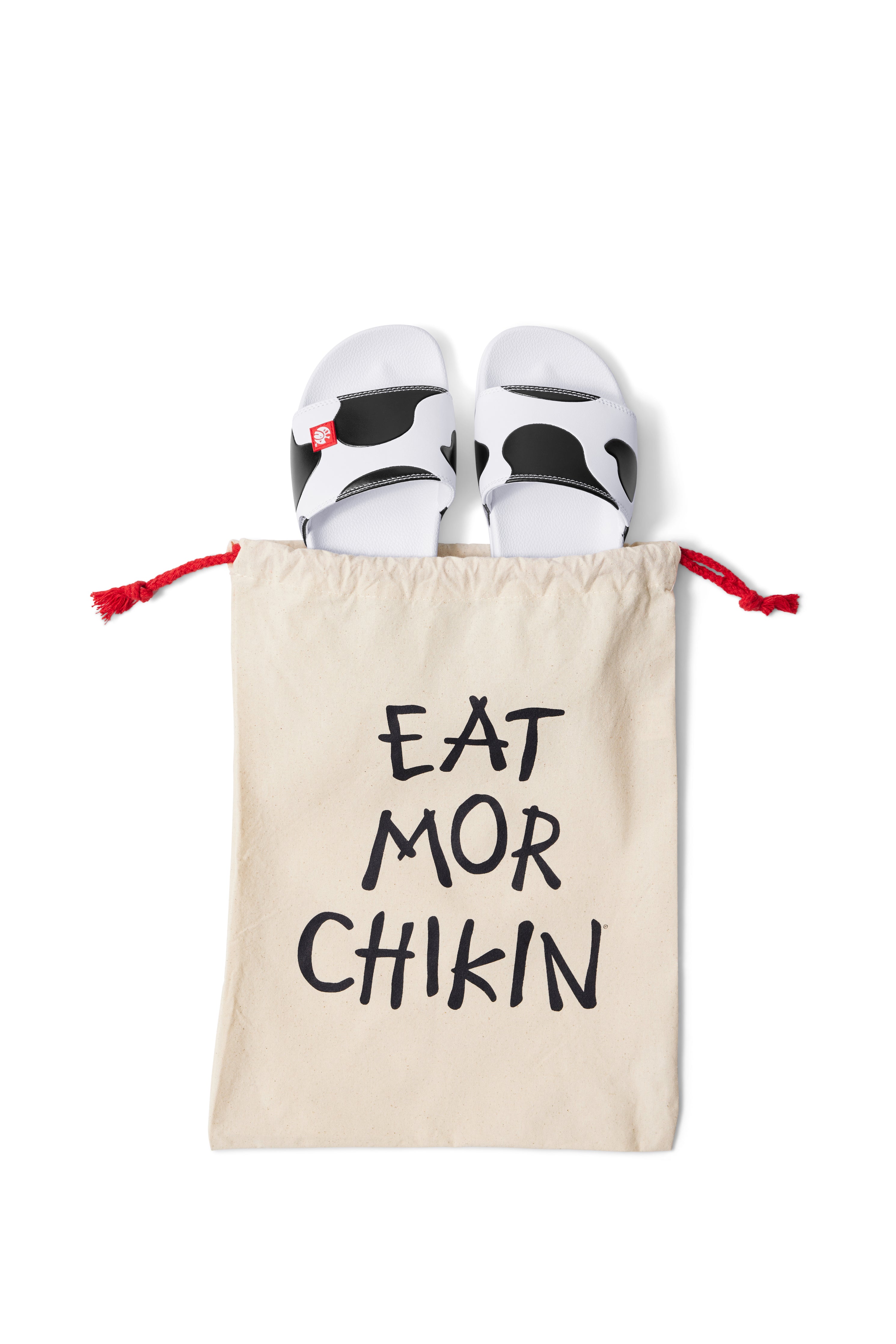 Overhead photograph of Slip On Cow Slides in natural canvas and black &quot;Eat Mor Chikin&quot; drawstring bag