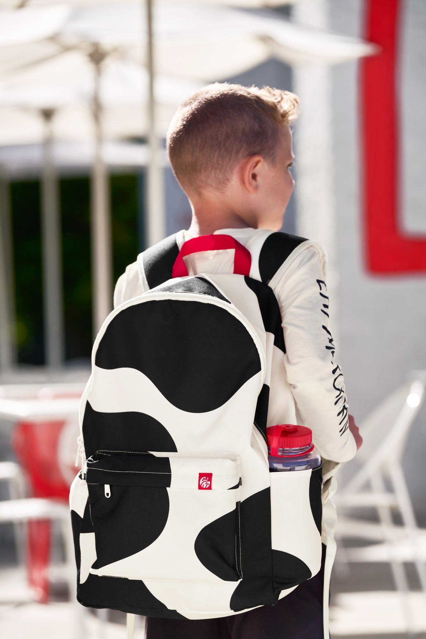 Boy wearing black and white Cow Print Backpack with red strap