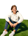 Man with blonde hair sitting on green turf wearing Lightweight Cow Pullover hoodie