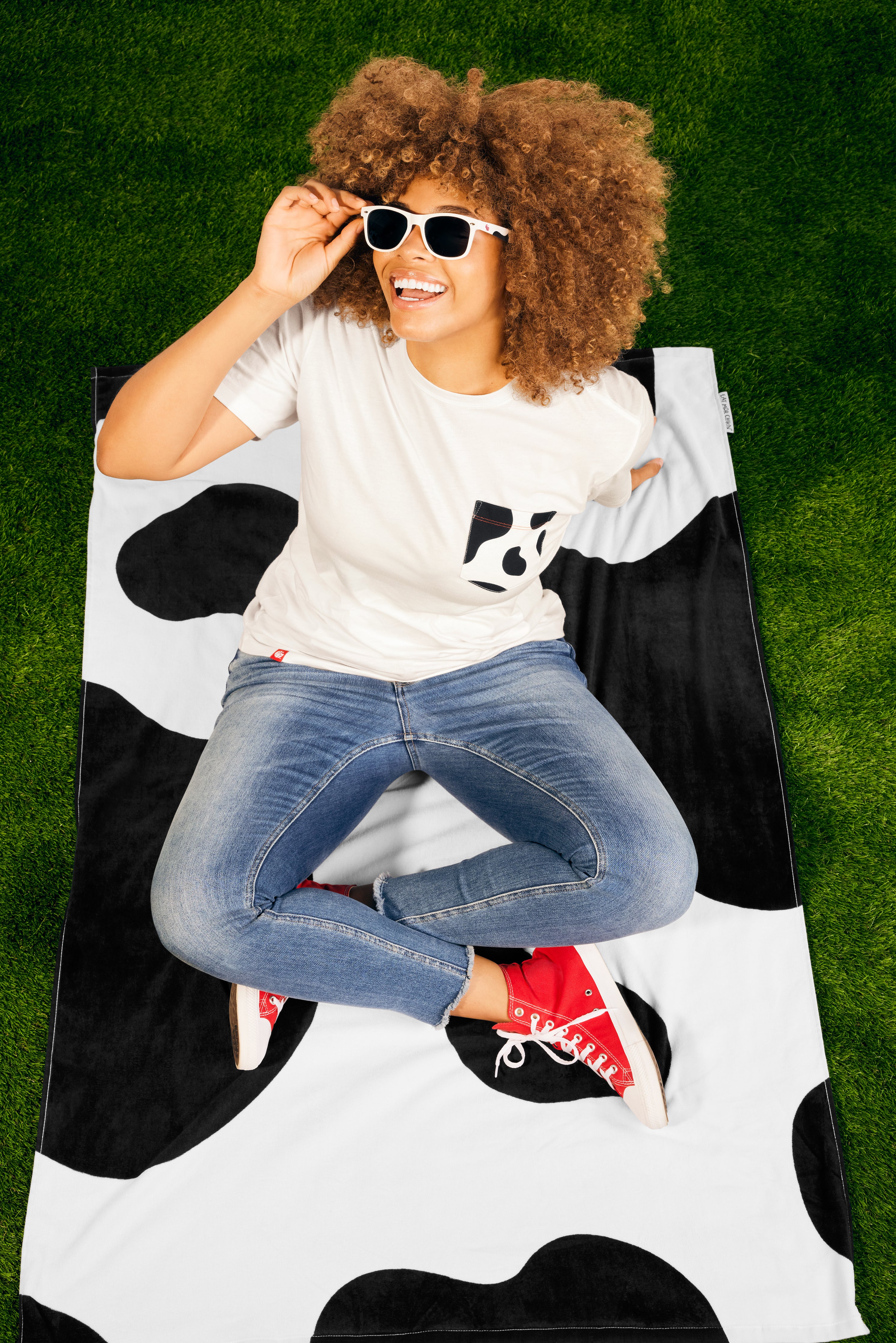 Woman sitting on black and white cow print Laze and Graze Beach Towel.