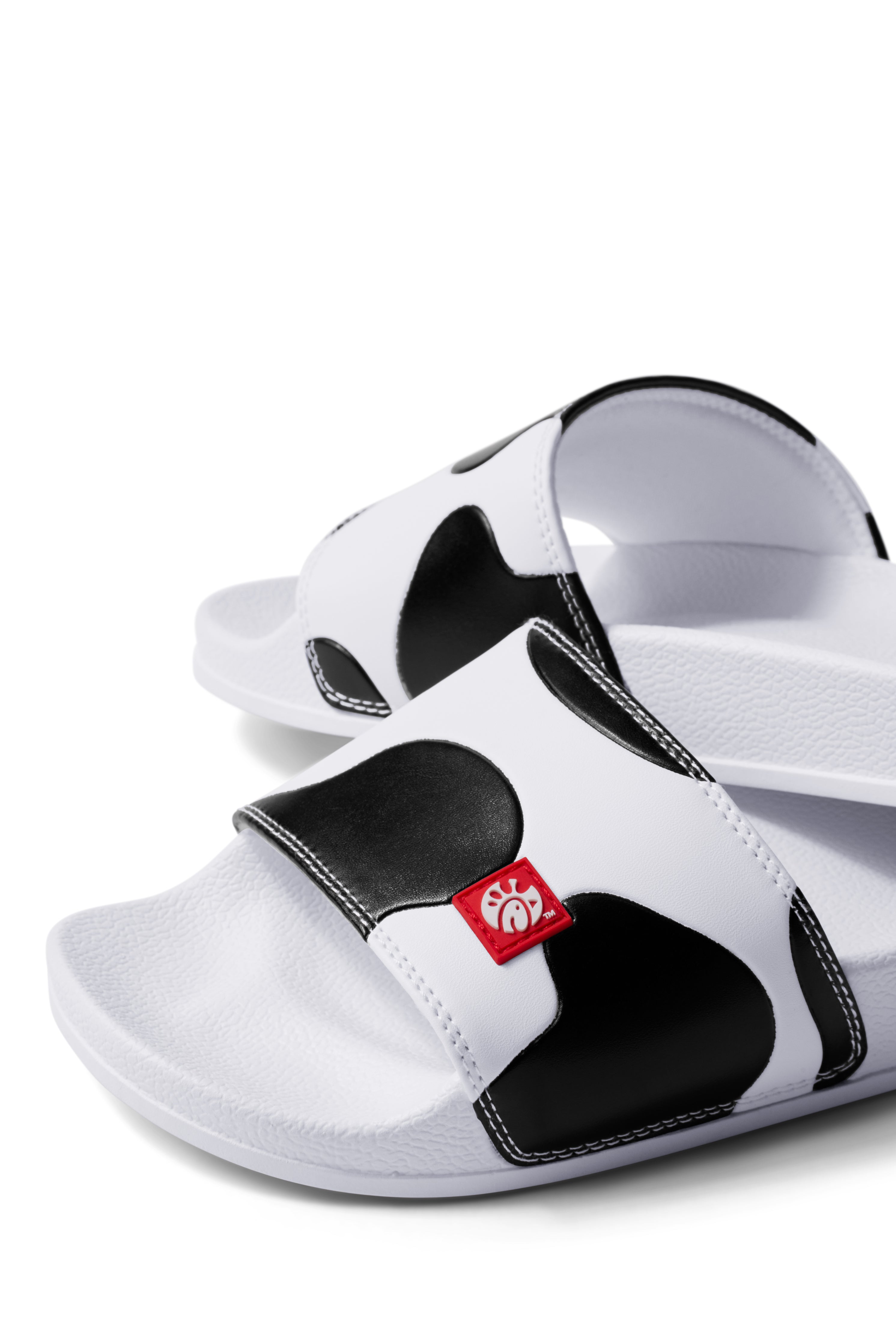 Close up view of Slip On Cow Slides showing black and white cow print pattern and red silicone logo label