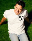 Man with brunette hair sitting on green turf wearing Cow Print Pocket Tee.