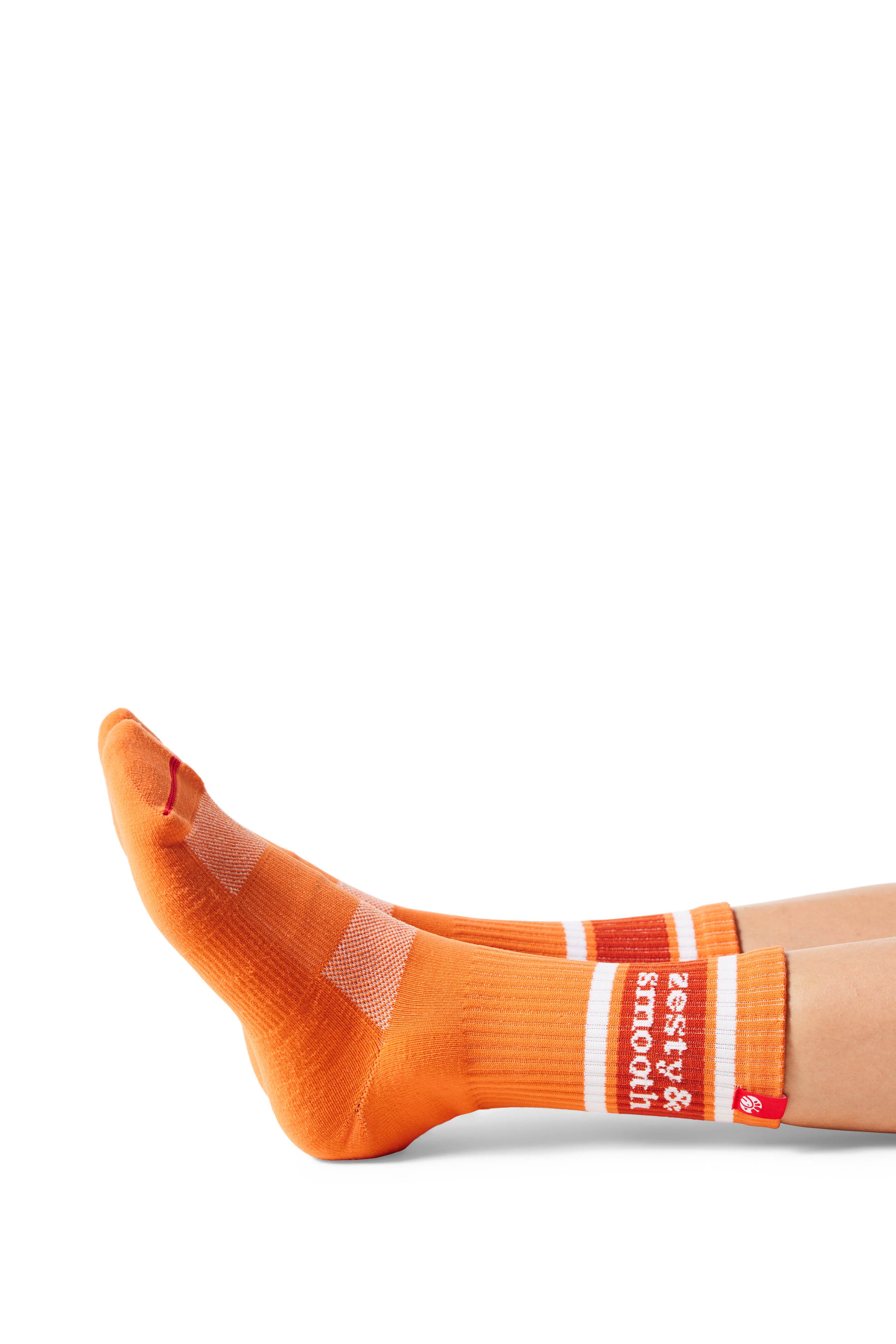 Pair of feet wearing orange socks with text &quot;zesty &amp; smooth&quot; above ankle on sock