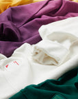 Closeup of silicone sauce patch on yellow, purple, gray/white, and green Ombre Crewnecks laying in a row