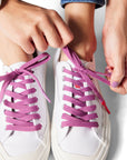 Closeup of someone tying purple shoelaces on white shoes