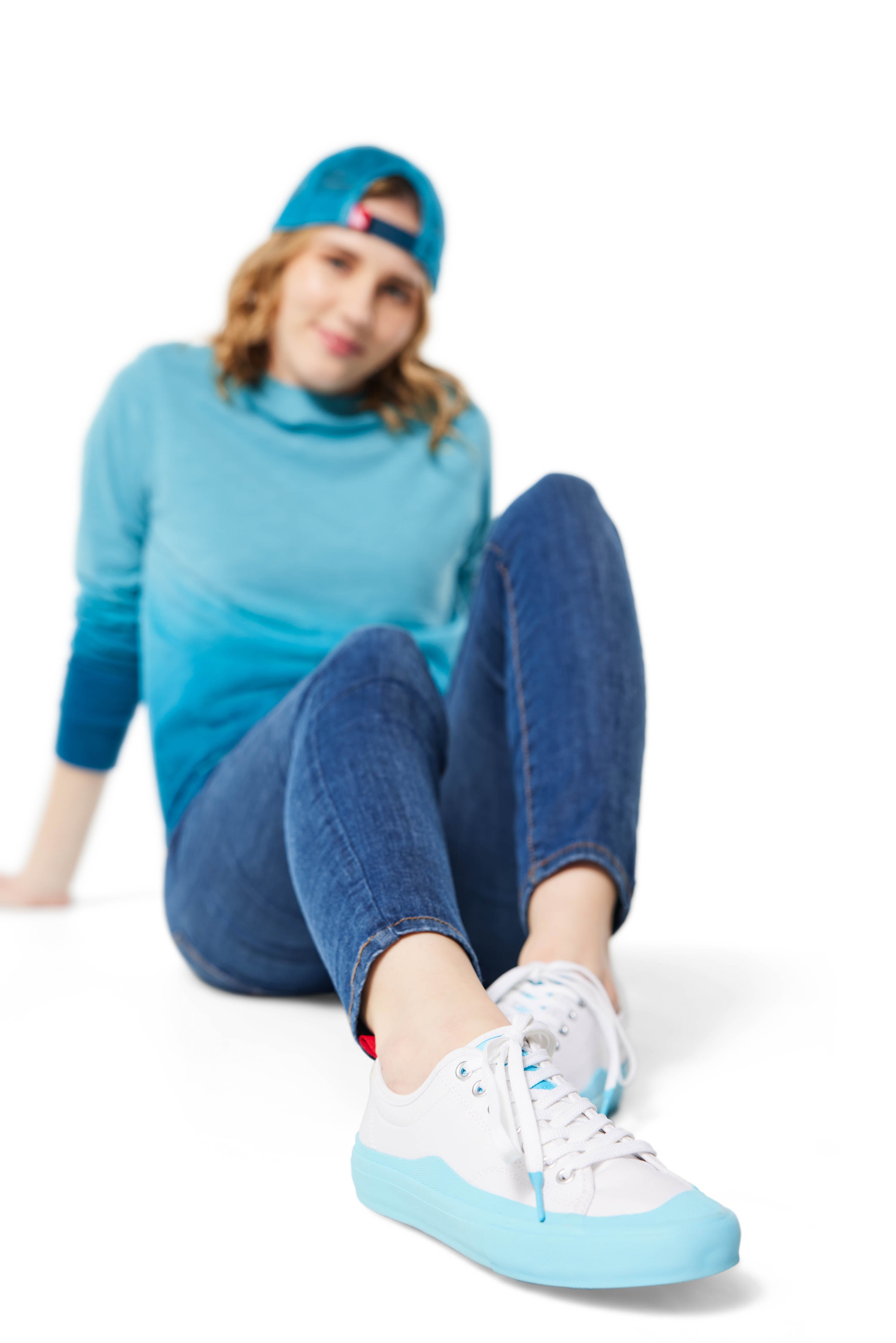 Woman sitting on ground wearing blue Ombre Crewneck with blue Dipped Kicks and blue Trucker Hat