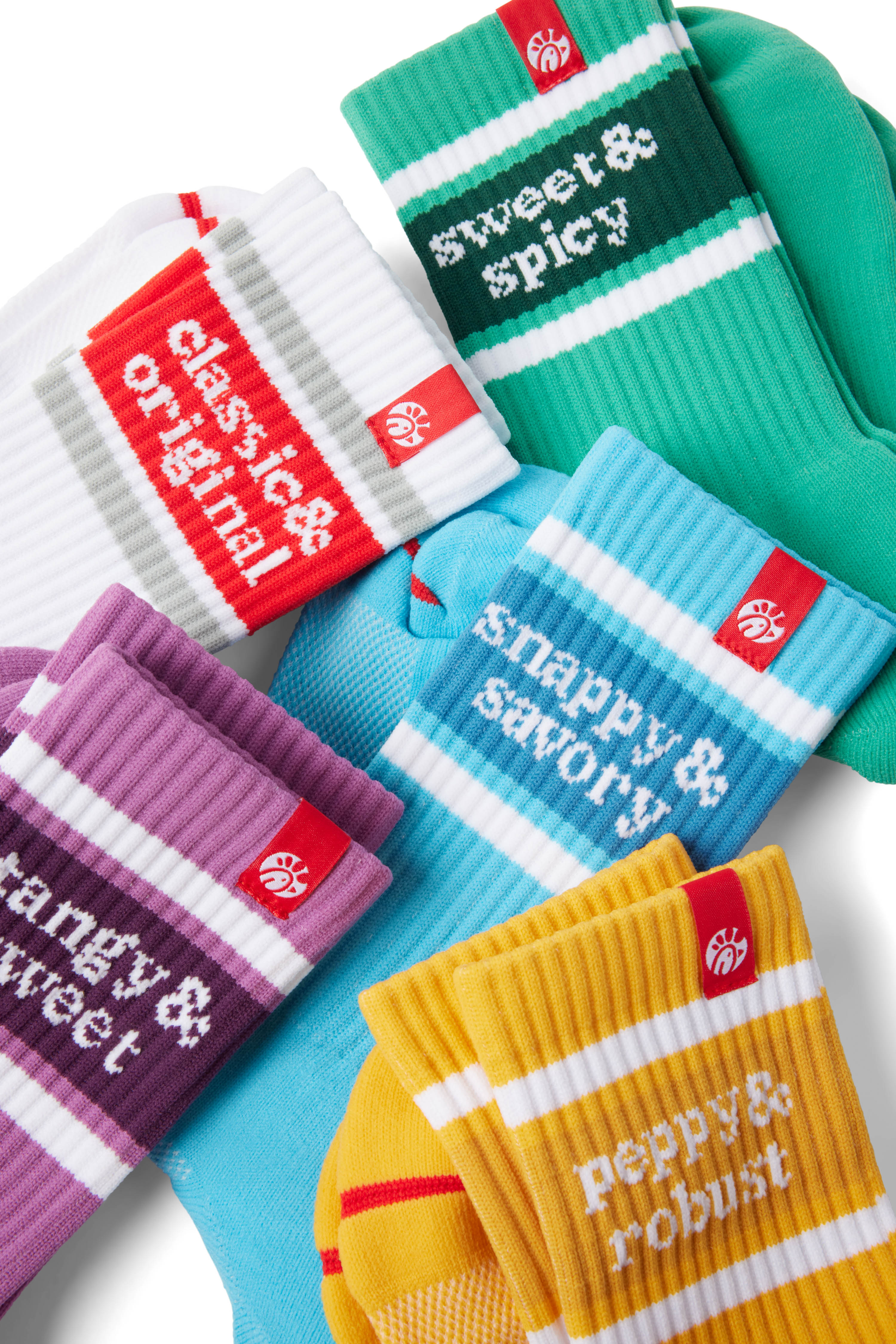 Closeup of several pairs of Socks: purple (tangy & sweet), yellow (peppy & robust), blue (snappy & savory), white/red, and green