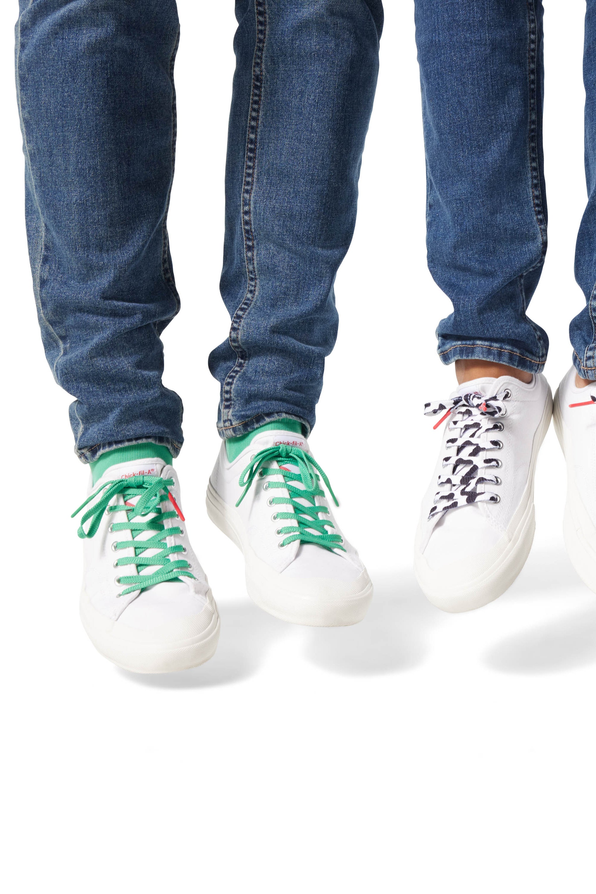 Two sets of Dipped Kicks shoes jumping in mid air displaying Sauce Shoelaces in green and cow print