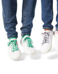 Two sets of Dipped Kicks shoes jumping in mid air displaying Sauce Shoelaces in green and cow print