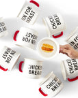 Overhead photograph of person holding Chicken for Breakfast Camper Mug and several other Chicken for Breakfast Camper Mugs laid on their sides