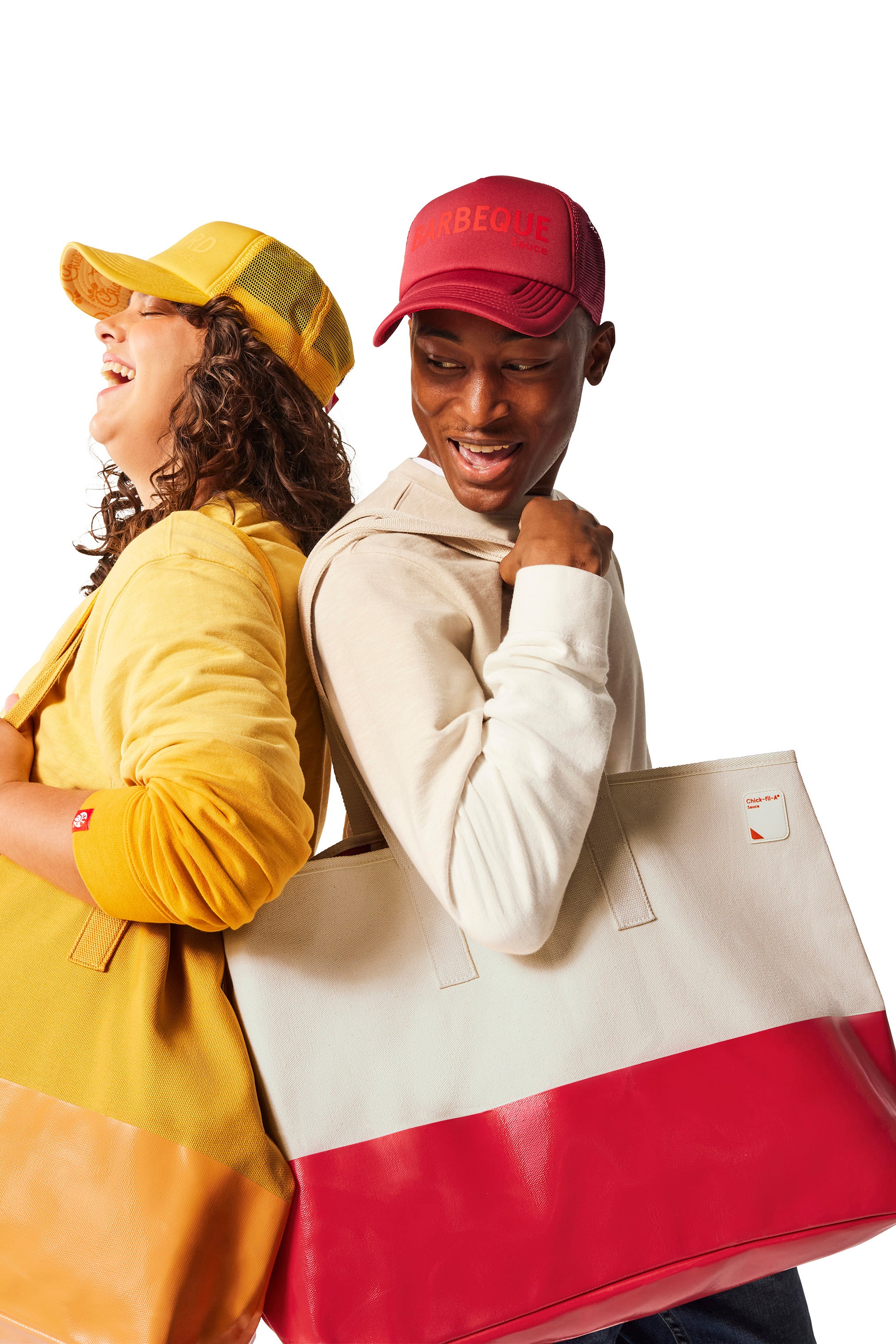 Woman wearing yellow Trucker Hat and yellow Tote Bag standing next to man with red Trucker Hat and red and canvas Tote Bag