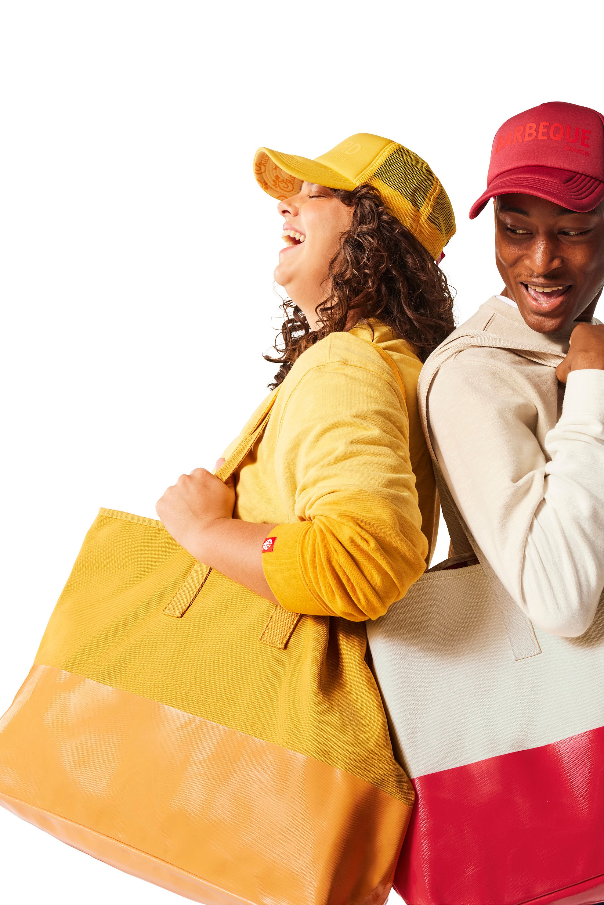 Woman wearing yellow Trucker Hat and yellow Tote Bag standing next to man with red Trucker Hat and red and canvas Tote Bag