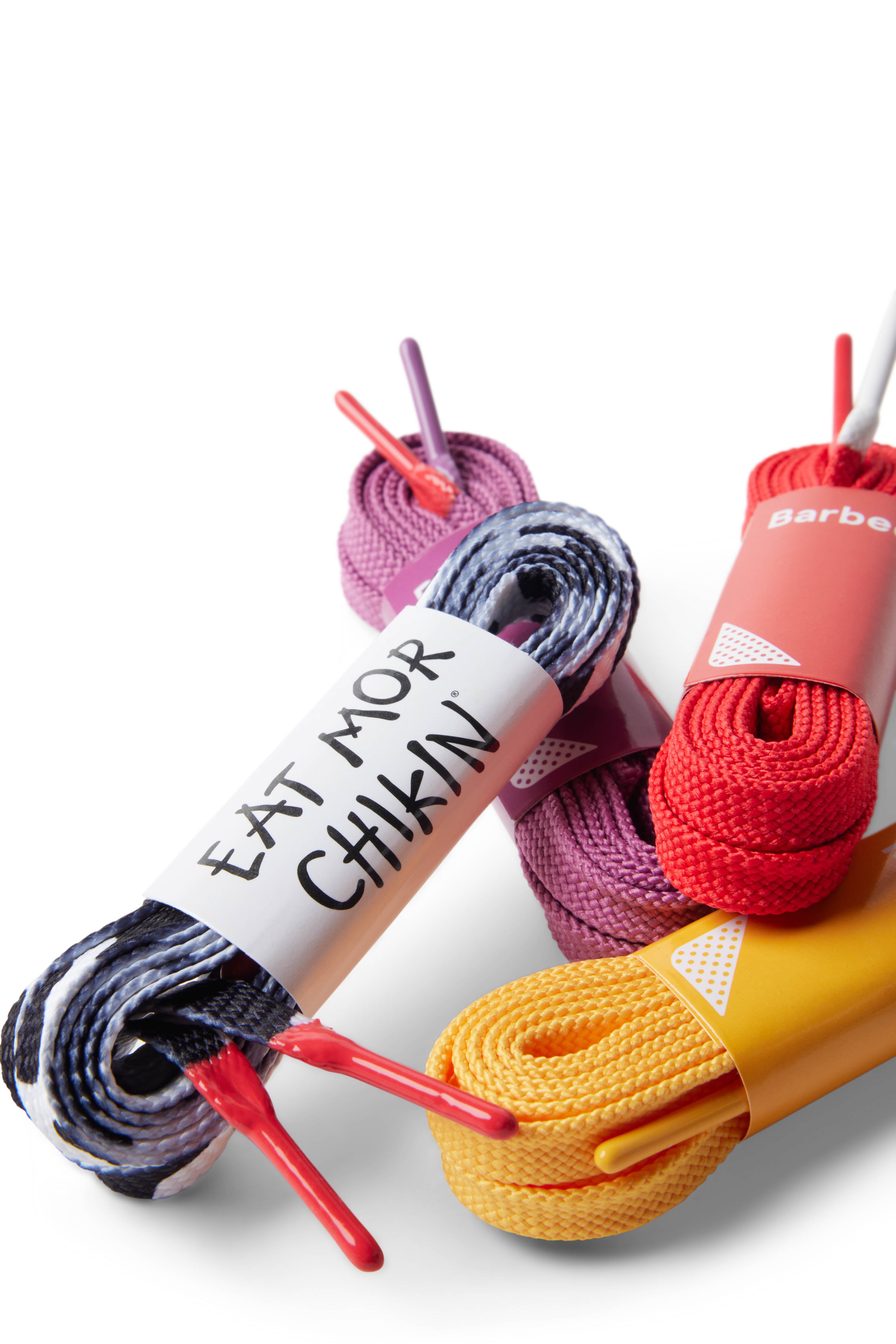 Four sets of shoelaces in a pile featuring cow print with Eat Mor Chikin packaging, yellow, red, and purple