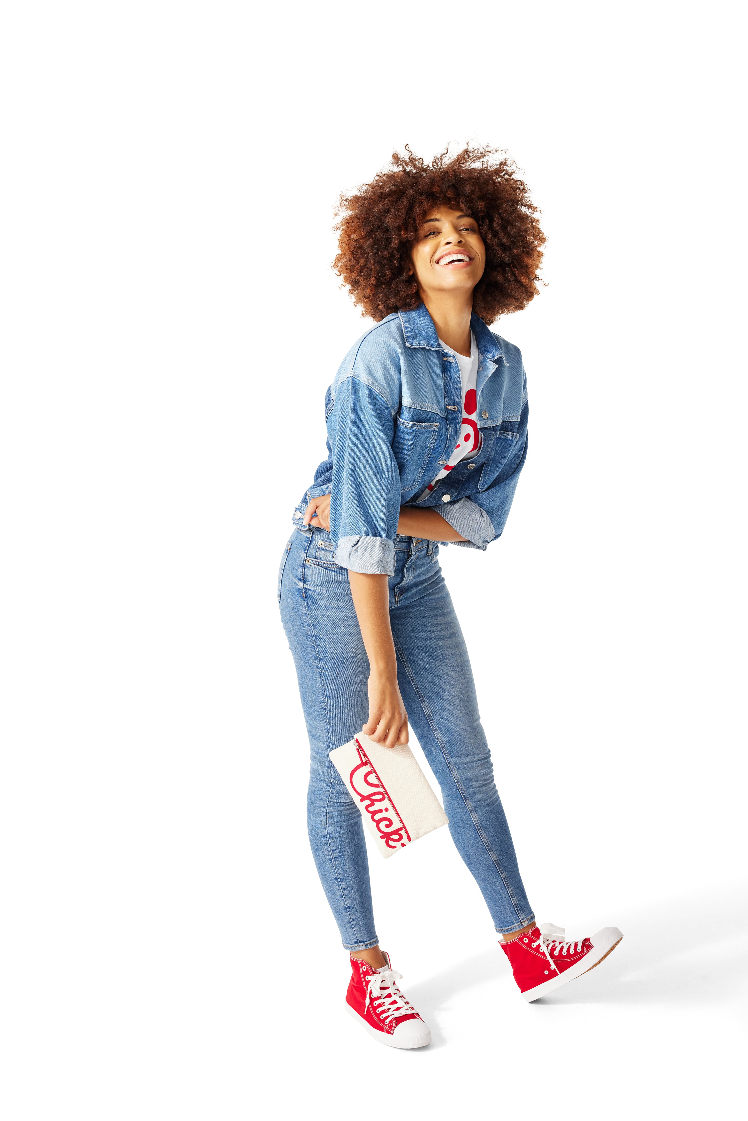 Woman standing and wearing jeans, denim jacket and white Classic Chick-fil-A® Tee and holding Classic Chick-fil-A™ Clutch