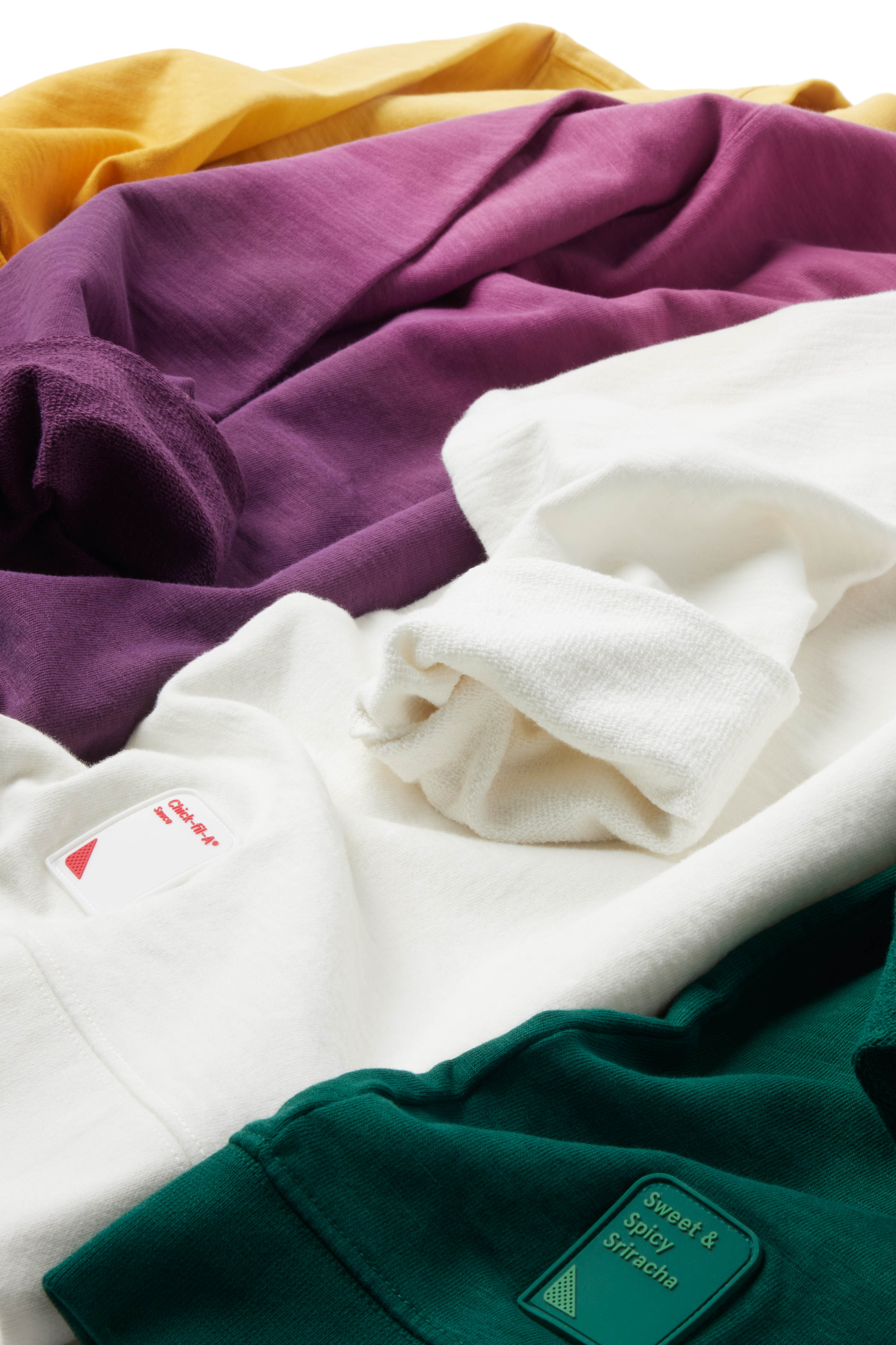 Closeup of silicone sauce patch on yellow, purple, gray/white, and green Ombre Crewnecks laying in a row