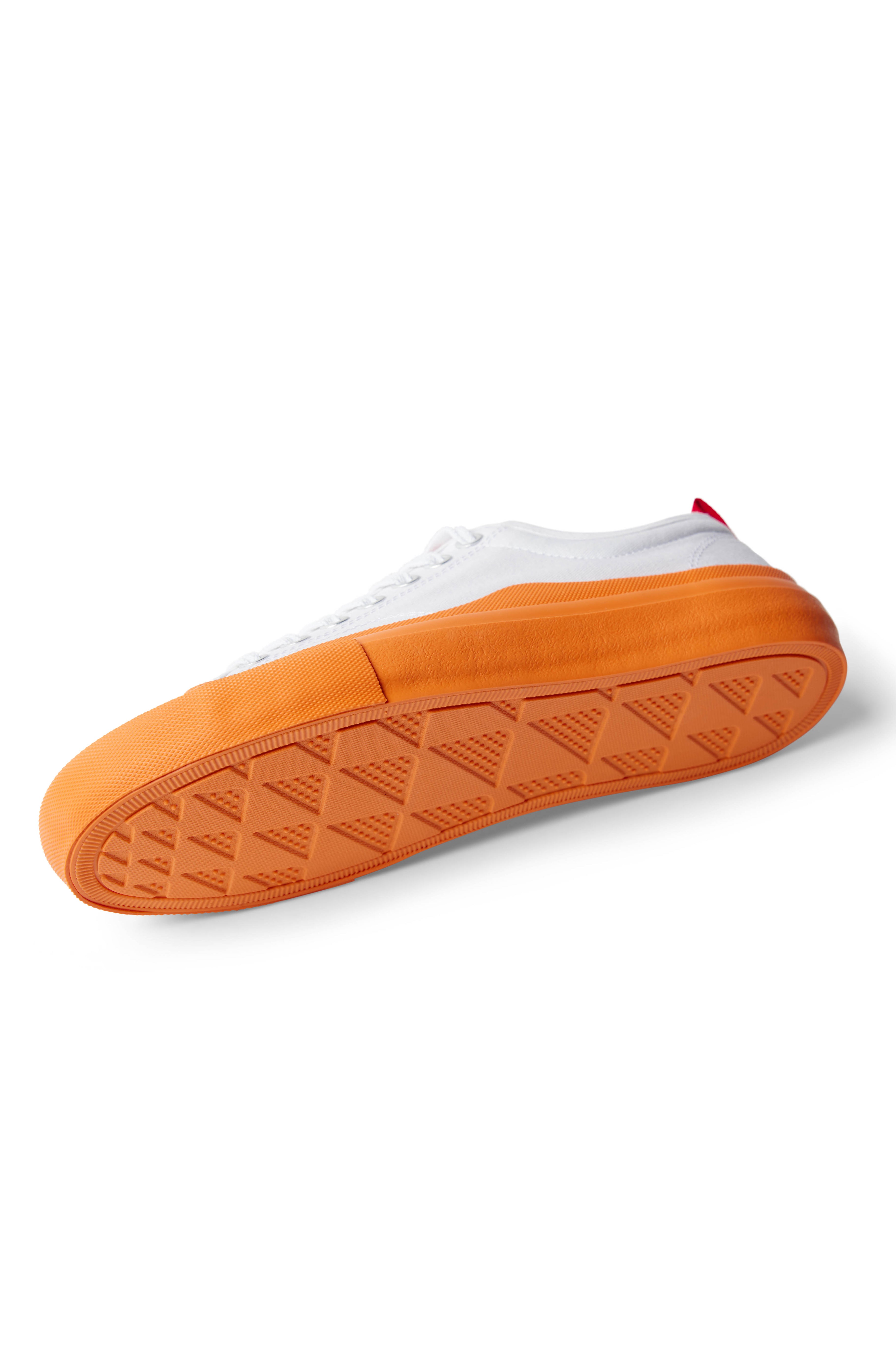 Side view of the bottom tread of single Dipped Kicks white shoes with orange soles