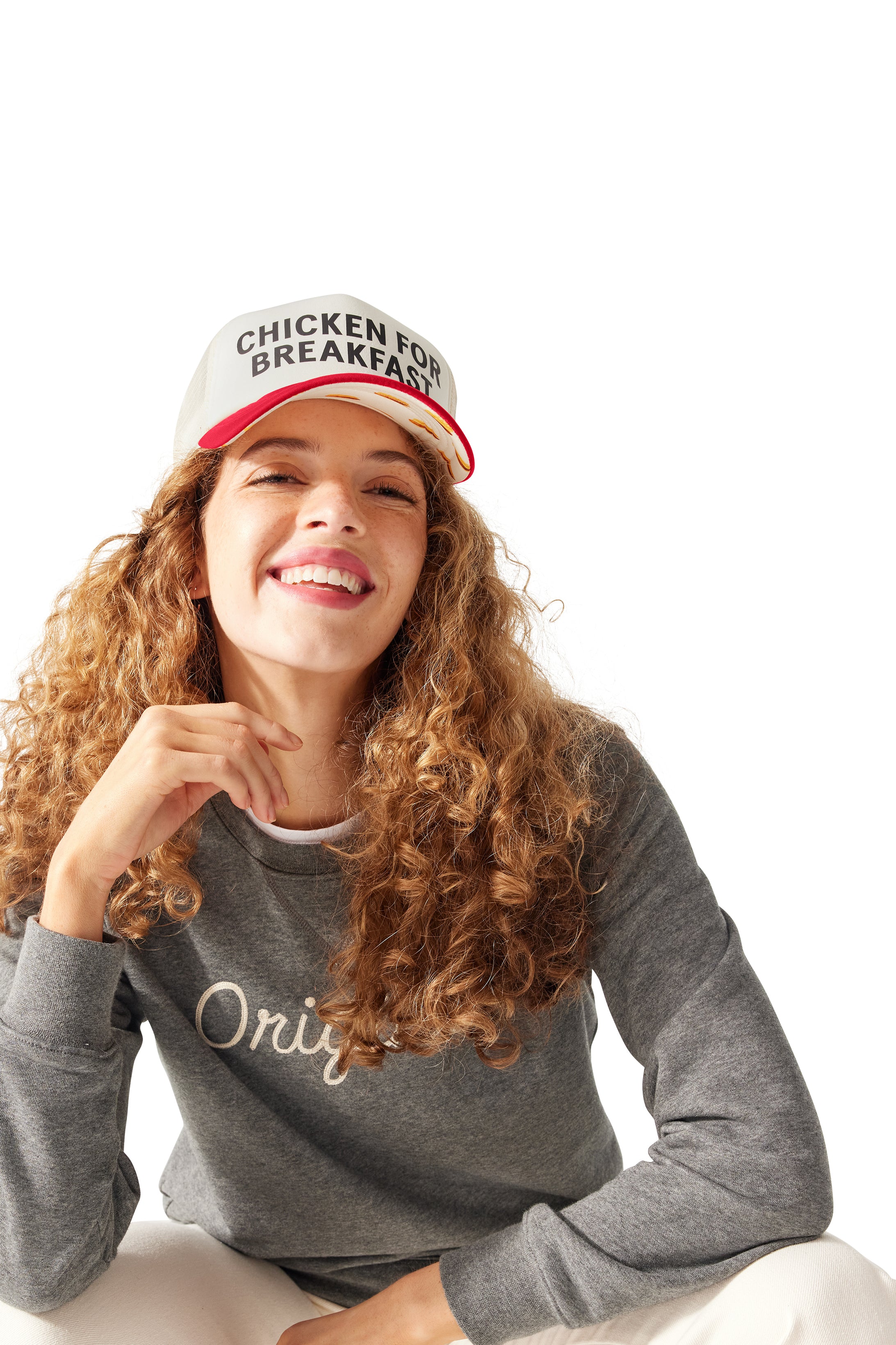 Woman squatting down and smiling, wearing Original Crewneck and Chicken for Breakfast Trucker Hat