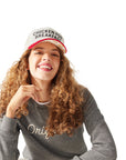 Woman squatting down and smiling, wearing Original Crewneck and Chicken for Breakfast Trucker Hat